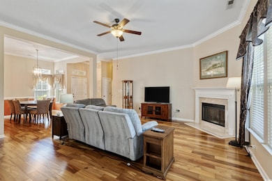 Living area featuring crown molding, light wood-style floors, a ceiling fan, a high end fireplace, and a chandelier