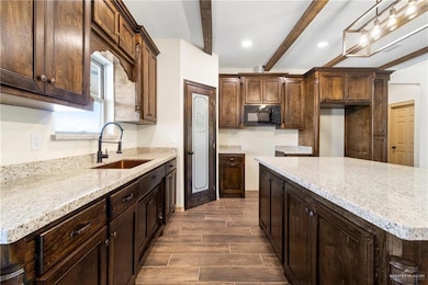 Kitchen featuring black microwave, wood tiled floor, dark brown cabinetry, beamed ceiling, and a sink