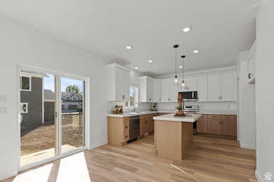 Kitchen featuring stainless steel appliances, white cabinetry, brown cabinetry, hanging light fixtures, and a center island.