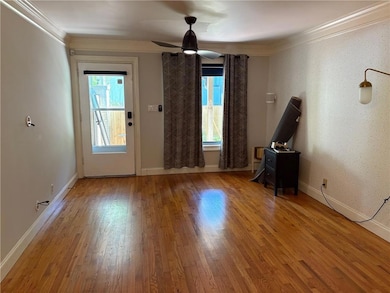 Unfurnished room featuring healthy amount of natural light, wood finished floors, ornamental molding, ceiling fan, and baseboards