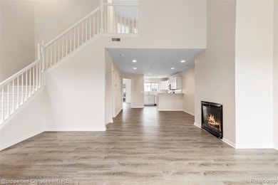 Unfurnished living room featuring a glass covered fireplace, a towering ceiling, recessed lighting, light wood-type flooring, and stairs