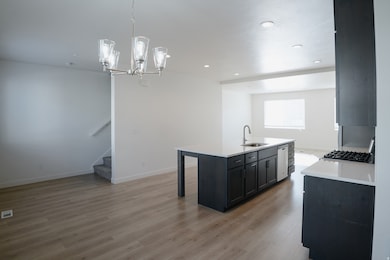 Kitchen featuring dark cabinets, a breakfast bar area, decorative light fixtures, a kitchen island with sink, and light wood finished floors