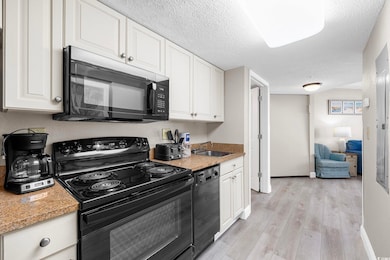 Kitchen featuring black appliances, white cabinets, a textured ceiling, light wood-style flooring, and light countertops