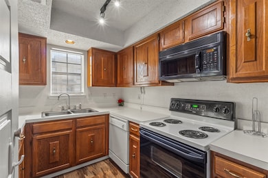 Kitchen with electric range, a textured ceiling, light countertops, black microwave, and brown cabinetry