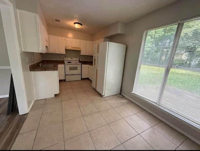 Kitchen featuring dark countertops, white appliances, white cabinetry, a textured ceiling, and light tile patterned floors