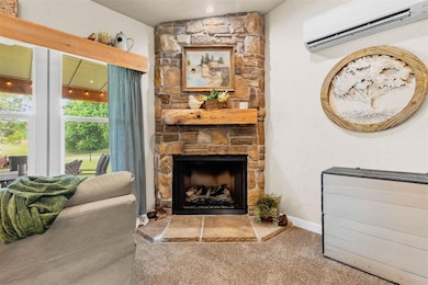 Carpeted living area with a wall mounted air conditioner, a stone fireplace, and baseboards