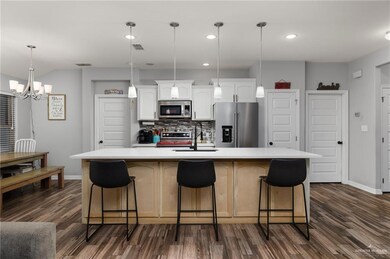 Kitchen with appliances with stainless steel finishes, white cabinetry, an island with sink, a kitchen breakfast bar, and hanging light fixtures