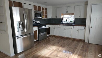 Kitchen featuring stainless steel appliances, dark countertops, wood finished floors, and white cabinets