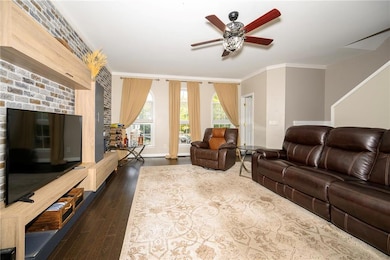 Living room with ceiling fan, ornamental molding, dark wood finished floors, and baseboards