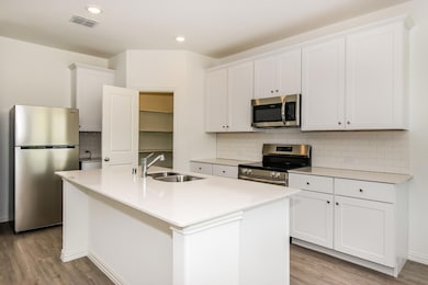Kitchen with appliances with stainless steel finishes, light hardwood / wood-style floors, white cabinetry, an island with sink, and sink