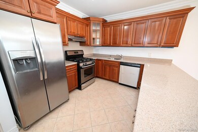 Kitchen with stainless steel appliances, brown cabinetry, light stone counters, light tile patterned floors, and crown molding