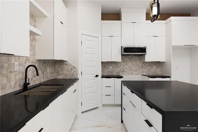 Kitchen with stainless steel microwave, light marble finish flooring, dark countertops, and tasteful backsplash