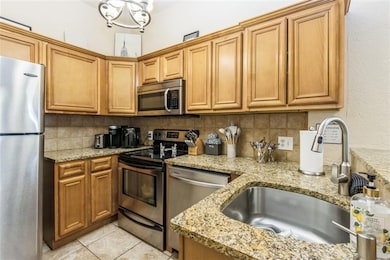 Kitchen featuring a sink, light tile patterned floors, backsplash, light stone counters, and appliances with stainless steel finishes