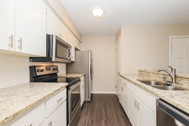 Kitchen featuring stainless steel appliances, light stone countertops, a textured ceiling, dark wood-style floors, and white cabinetry