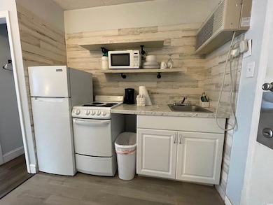 Kitchen featuring white appliances, a sink, white cabinetry, wood finished floors, and wood walls
