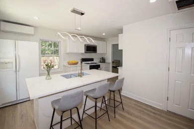 Kitchen featuring white appliances, a wall mounted AC, light wood-style flooring, white cabinetry, and a breakfast bar area