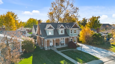 View of front of house with covered porch, a front yard, a chimney, and brick siding