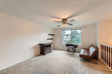 Living area with a ceiling fan, light colored carpet, baseboards, and a textured ceiling
