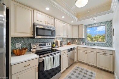 Kitchen featuring appliances with stainless steel finishes, a sink, light wood finished floors, decorative backsplash, and a tray ceiling