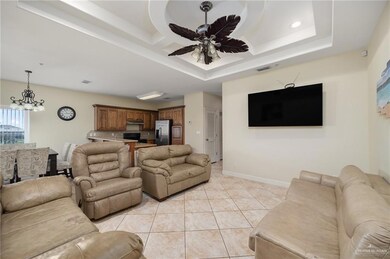 Living room featuring ceiling fan with notable chandelier, light tile patterned floors, and a tray ceiling
