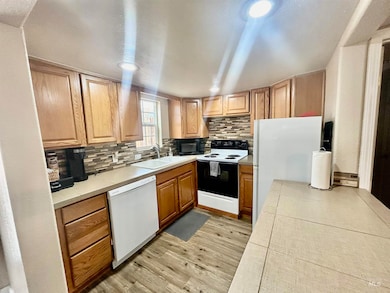 Kitchen with light wood-style flooring, decorative backsplash, white appliances, and light countertops
