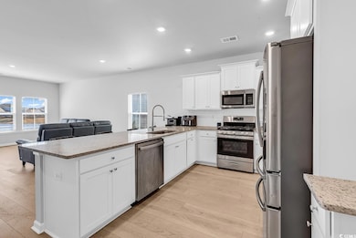 Kitchen with stainless steel appliances, white cabinetry, open floor plan, recessed lighting, and light stone countertops