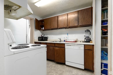 Kitchen featuring white appliances, light countertops, extractor fan, open shelves, and a textured ceiling