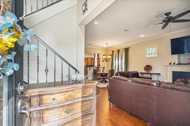 Living room featuring a tiled fireplace, hardwood / wood-style flooring, ceiling fan with notable chandelier, and crown molding