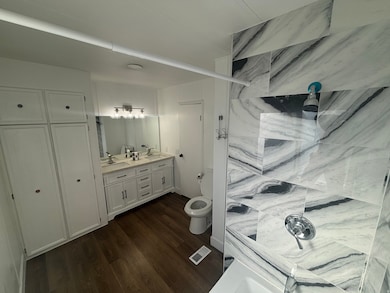 Bathroom with double vanity, dark wood-style flooring, and tiled shower