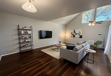 Living room with dark wood-type flooring, ceiling fan, and high vaulted ceiling