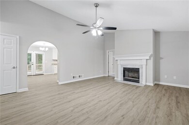 Unfurnished living room with arched walkways, high vaulted ceiling, a ceiling fan, a chandelier, and light wood finished floors