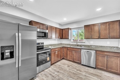 Kitchen with stainless steel appliances, light stone countertops, light wood-style floors, and recessed lighting