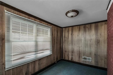 Unfurnished room featuring wooden walls and dark colored carpet