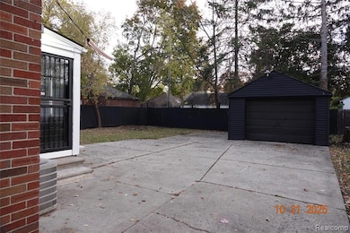Fenced backyard with a patio area, driveway, an outbuilding, and a detached garage