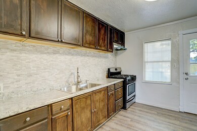 Cute and quaint kitchen has natural stone tile backsplash, stainless sink and a gas range with a great view of the back porch