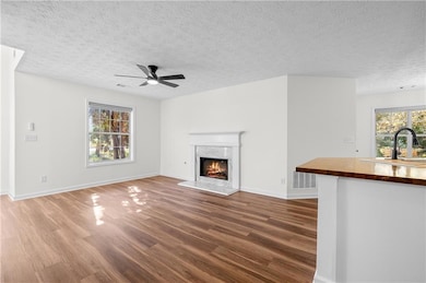 Unfurnished living room with dark wood finished floors, a premium fireplace, a textured ceiling, and ceiling fan