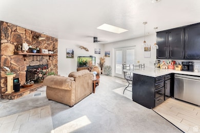 Living room featuring a stone fireplace, a skylight, french doors, a textured ceiling, and light carpet