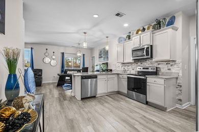 Kitchen featuring appliances with stainless steel finishes, a peninsula, decorative backsplash, light wood-type flooring, and white cabinetry