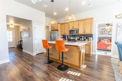 Kitchen featuring pendant lighting, dark wood-type flooring, appliances with stainless steel finishes, backsplash, and a center island with sink