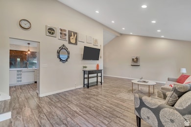 Living room with light wood finished floors, beam ceiling, recessed lighting, and high vaulted ceiling