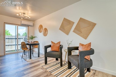 Living area featuring an AC wall unit, baseboards, wood finished floors, and a chandelier