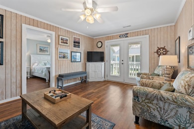 Living room with a ceiling fan, ornamental molding, french doors, wood finished floors, and wooden walls