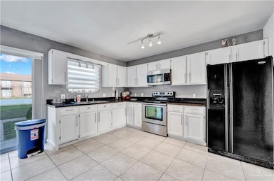 Kitchen with stainless steel appliances, a sink, white cabinetry, and light tile patterned floors