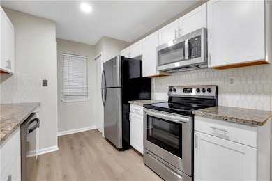Kitchen with appliances with stainless steel finishes, light wood finished floors, white cabinetry, and tasteful backsplash
