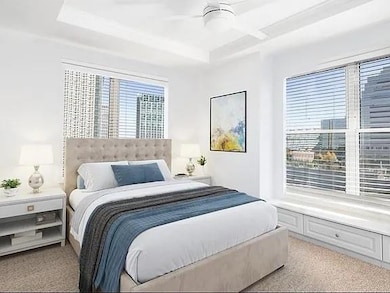 Bedroom with light colored carpet, a raised ceiling, and a ceiling fan