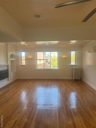 Unfurnished room featuring hardwood / wood-style floors, radiator, a ceiling fan, and a wall mounted AC