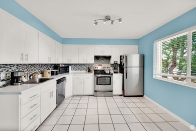 Kitchen with appliances with stainless steel finishes, decorative backsplash, light countertops, light tile patterned floors, and white cabinetry