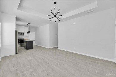 Unfurnished living room featuring a tray ceiling, a chandelier, baseboards, and light wood-style flooring