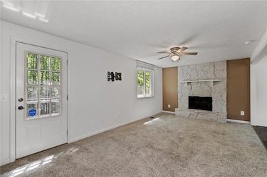 Unfurnished living room with a ceiling fan, a fireplace, carpet floors, and a textured ceiling