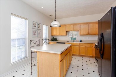 Kitchen with black appliances, light countertops, a center island, decorative light fixtures, and a breakfast bar